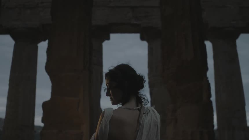 A woman standing near greek ruins at dusk