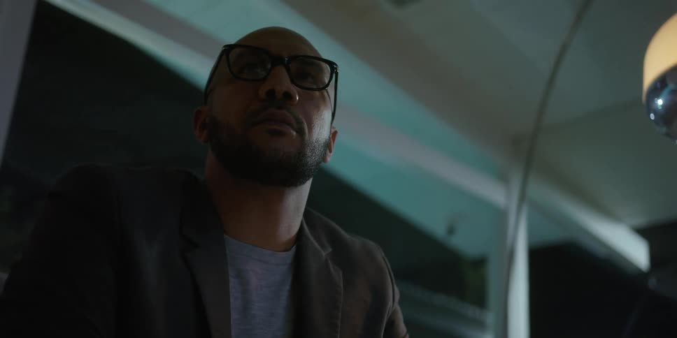 Bearded bald man wearing glasses sitting on a couch at home stands up and walks out of frame