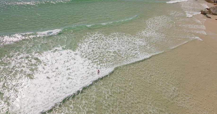 A man paddles out to catch a wave on a surfboard while a person wades close to shore