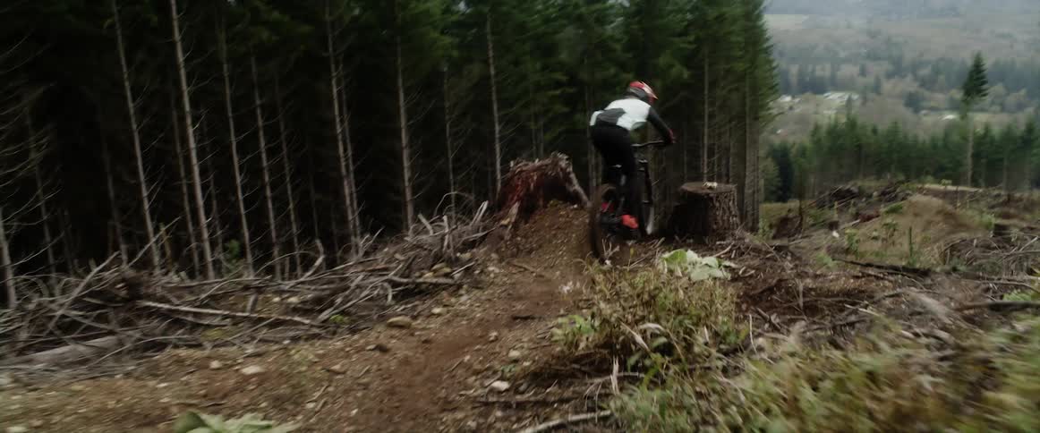 Cyclist with helmet jersey and pants rides bicycle downhill next to forest