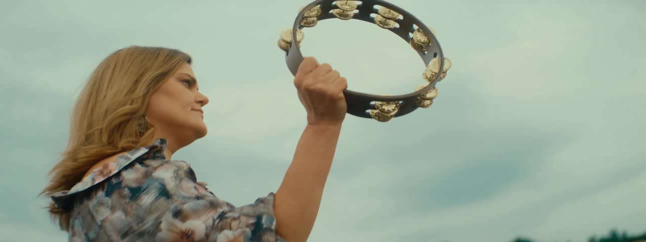 A woman swings and plays a tambourine as she dances outside
