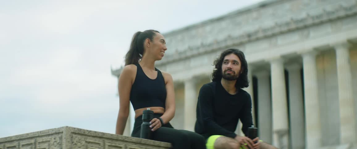 A man and woman sitting on a wall holding water bottles laughing and talking
