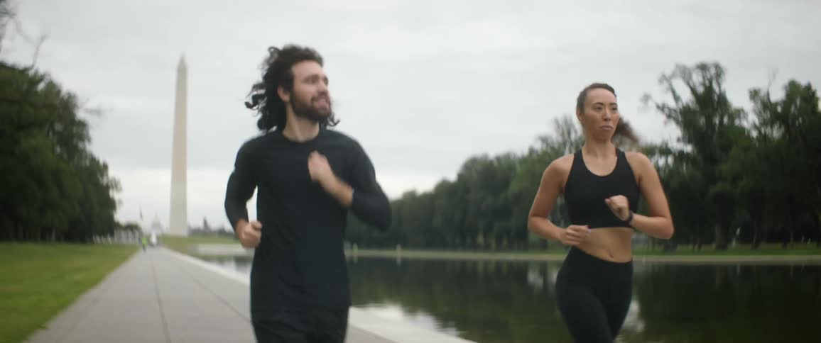 Man and woman jog along pathway near water with washington monument in the background