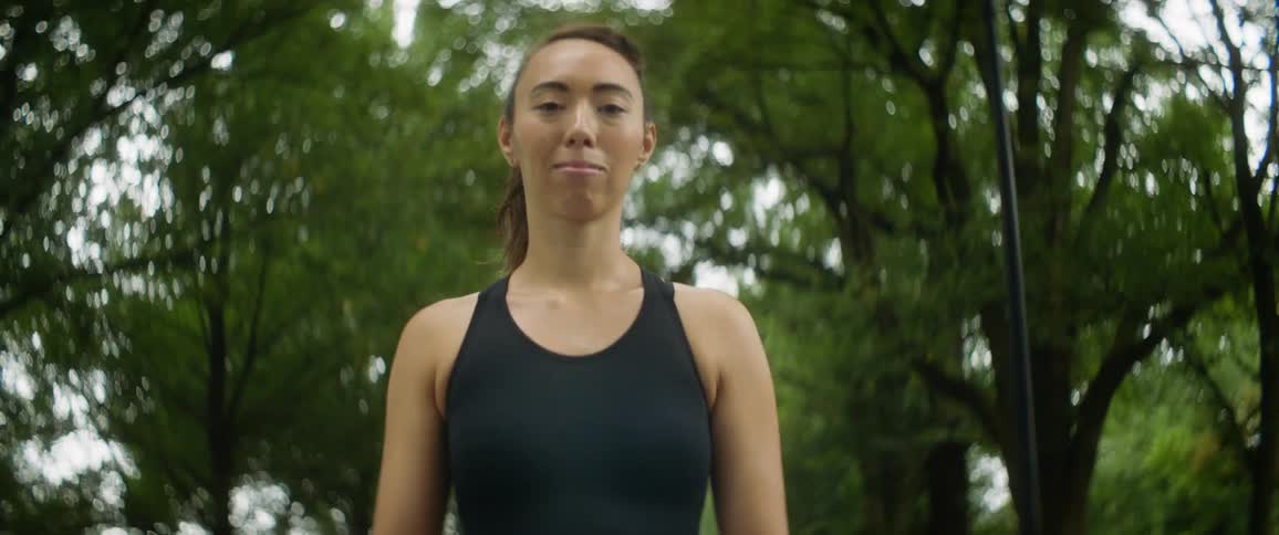 Woman wearing sports top smiles while walking outdoorson path under trees