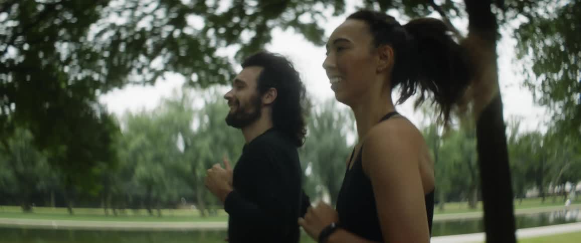 A man and woman talk while jogging together through a park during the day