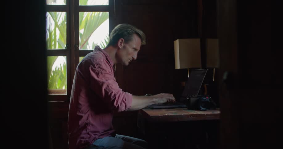A man types on a laptop then leans forward looking at the screen