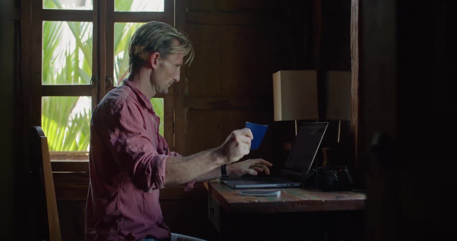 A man opens his passport to type something on his laptop