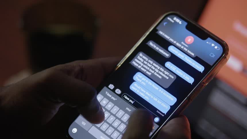 Person sitting near laptop texts on smartphone