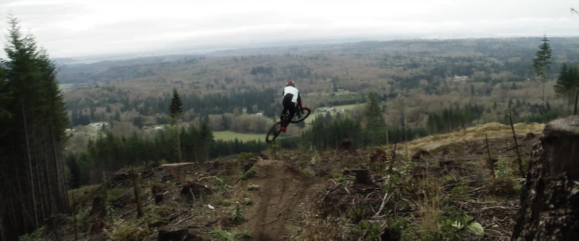 A person rides a motocross bike speeding down the slopes of a mountain near the pine tree forest