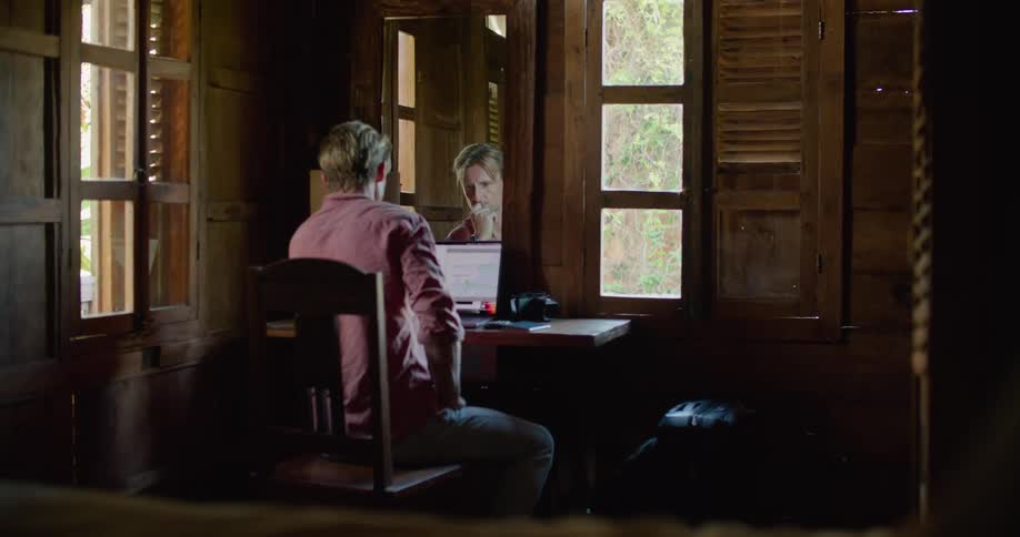 A man sits at home and thinks as he looks at his laptop and then types