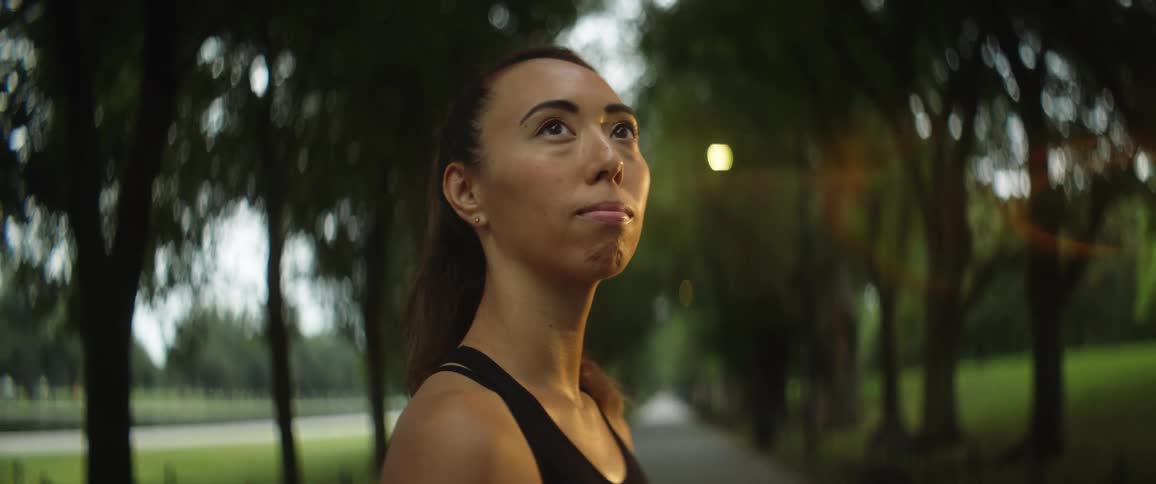 A woman is standing on a sidewalk in a park looking up