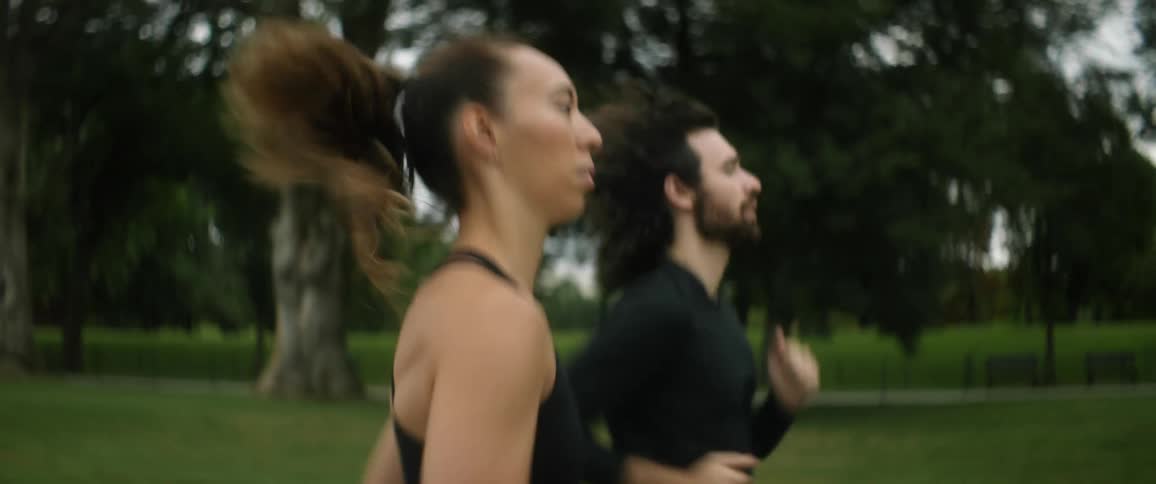 A man and woman jogging side by side in stride through the park
