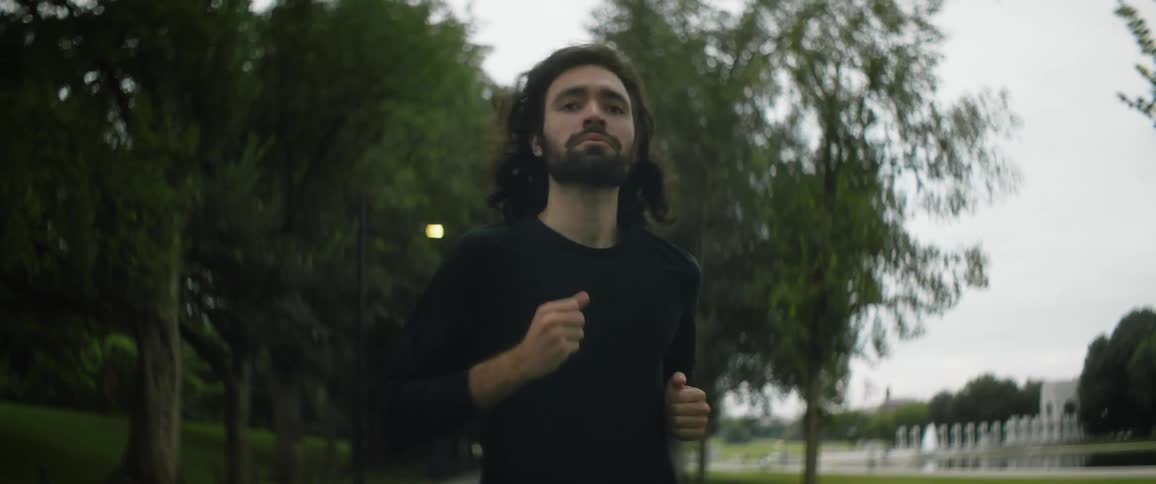 A man is jogging in a park running on a sidewalk surrounded by trees