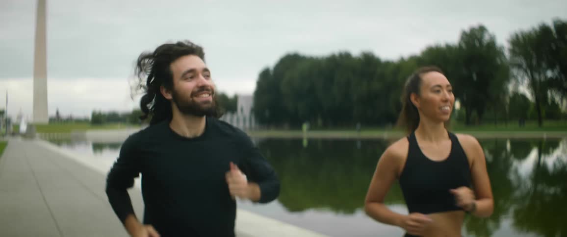 Man and woman jog along path near reflective pond with the washington monument in the background