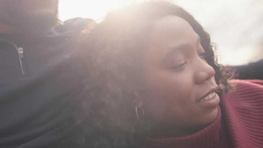Man whit beard and black top holds woman with curly hair earrings and red turtleneck sweater in the forest