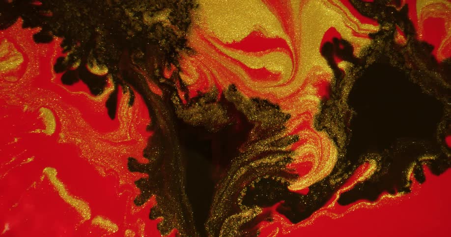 Drops of black break through a red and gold surface flowing and shimmering