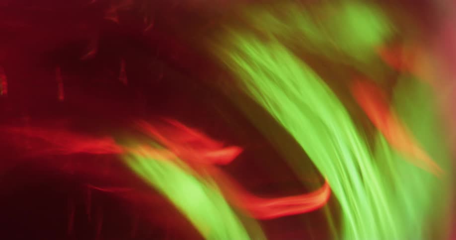 Light reflecting on colorful streaks of orange and green floating in liquid