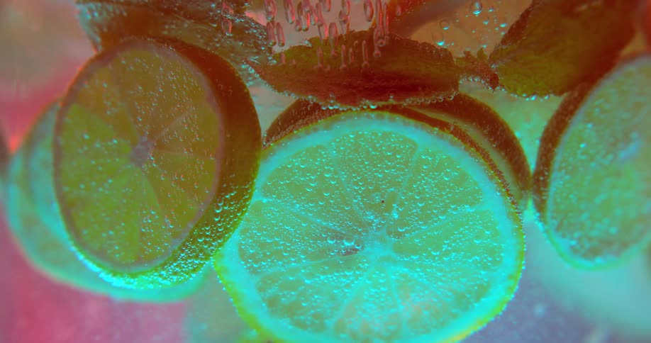 Slices of citrus fruit and mint leaves swirl around in a drink in a colorful display