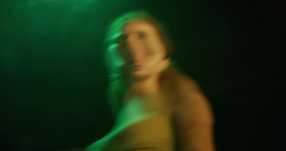 Woman standing under a bright green light at night reflecting on a pool of water