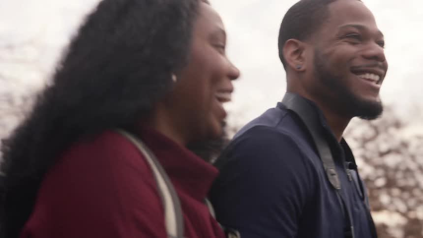 A man and woman chat and laugh while walking together outdoors on a cloudy day