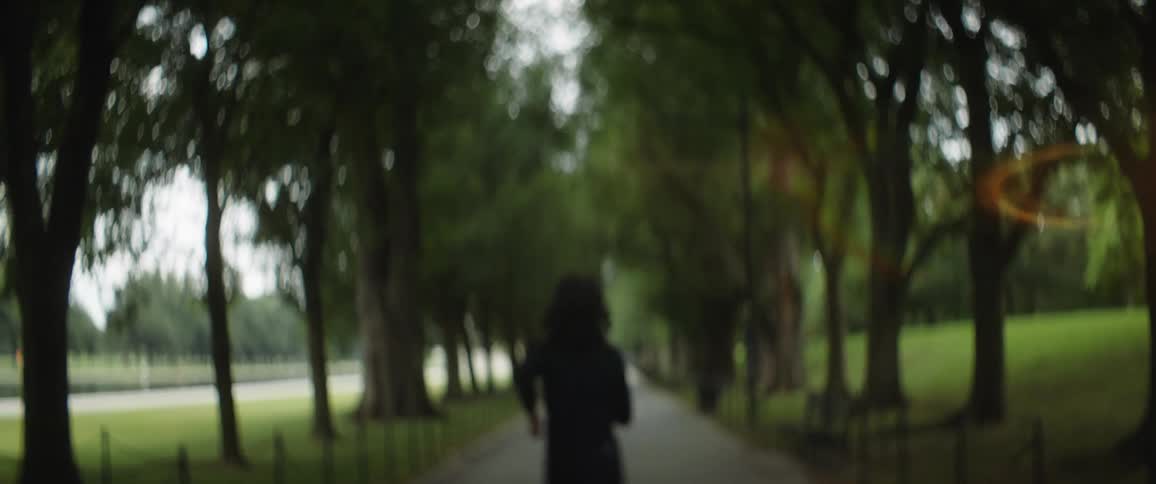 A man is standing on a sidewalk between trees in a park and he turns and runs