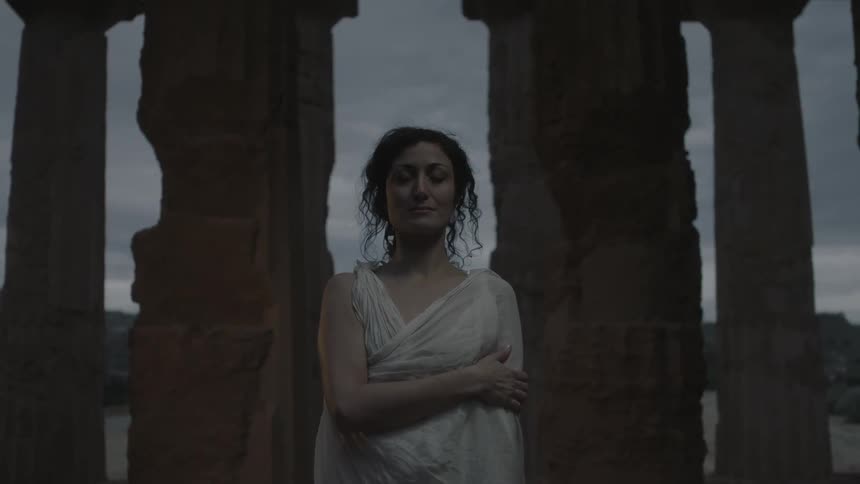 A woman stands by pillars at dawn