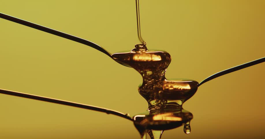 Honey is poured and flows onto stacked spoons against a yellow background