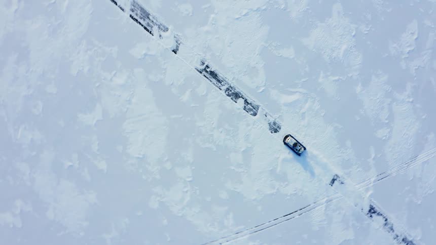 Aerial view of a hovercraft driving over the snow on an arctic landscape near the mountains