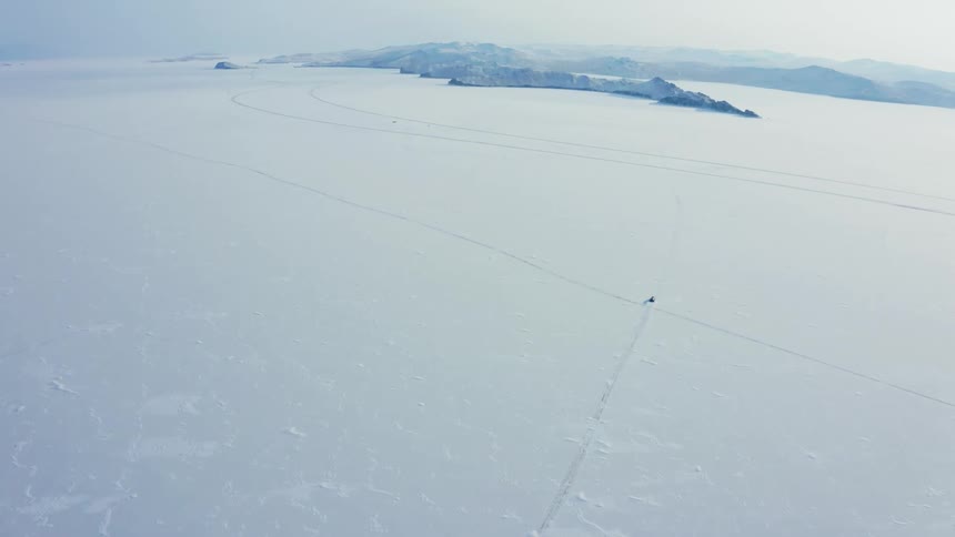 Aerial view of a hovercraft driving snowy lake on an arctic landscape near the mountains
