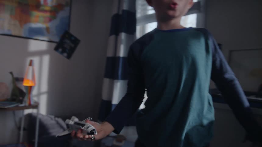 Boy stands in bedroom playing with a toy space shuttle