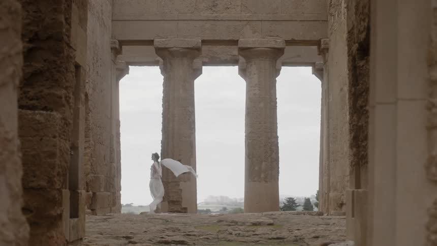 A woman in a flowing dress stands near a stone pillar