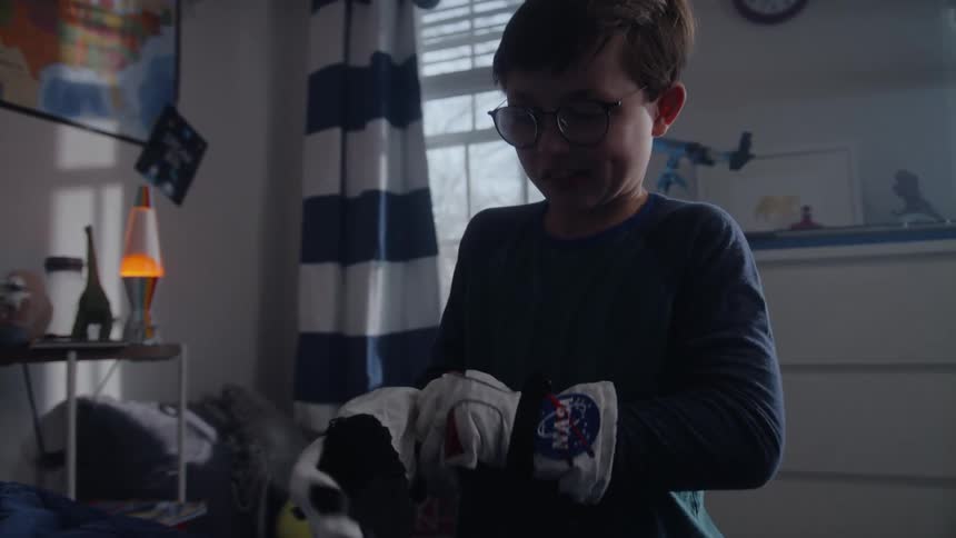 A smiling boy puts on a toy astronaut helmet and gloves before picking up a toy