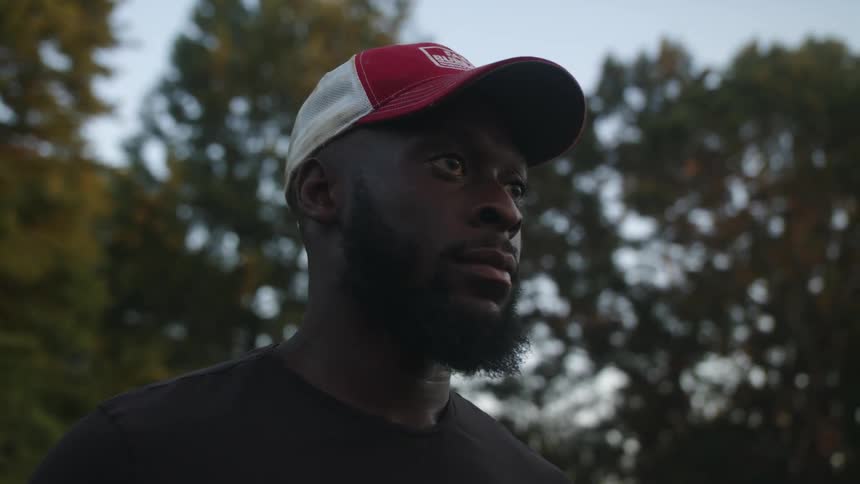 Man with white and red cap beard and black t shirt looks around in the forest