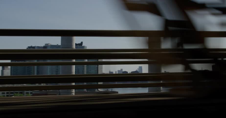 Moving over a bridge tall buildings and factories line the harbor under a clear sky