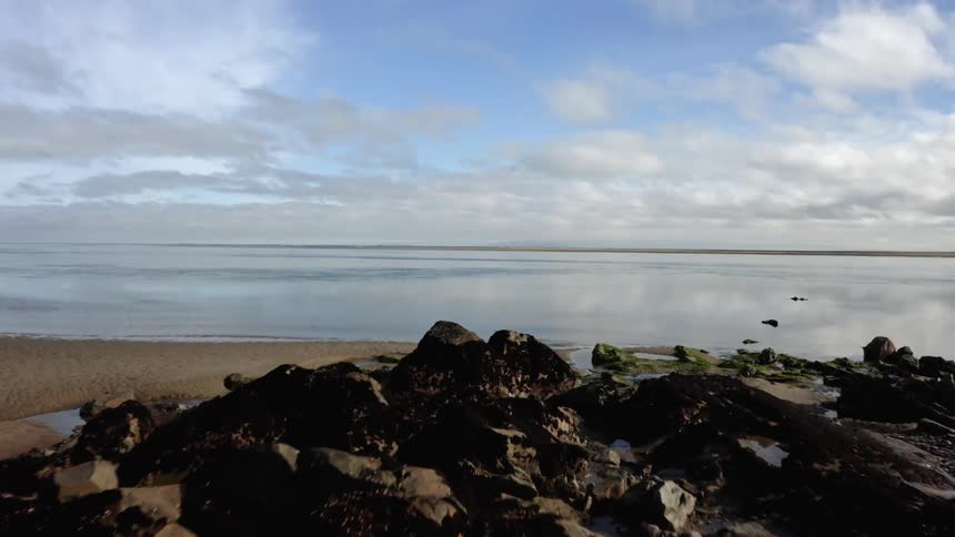 A low aerial view of a rocky beach and calm estuary