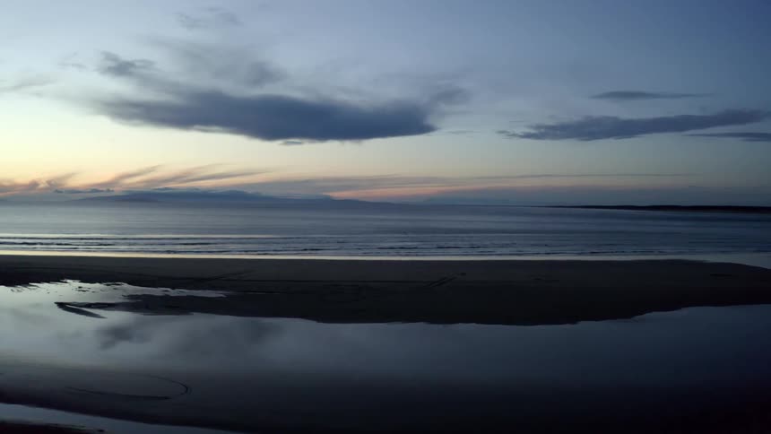 A sandy beach at sunrise reflecting pools of water