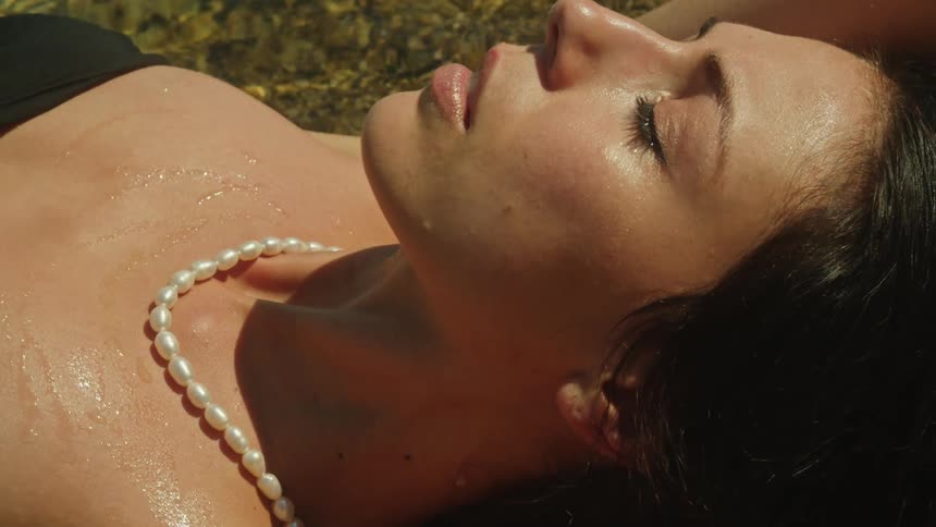 A woman wearing makeup and pearl necklace lying on the sand posing in the water