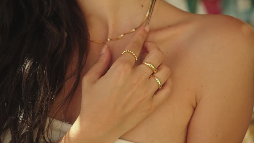 Woman poses lifting hand to show rings and necklace