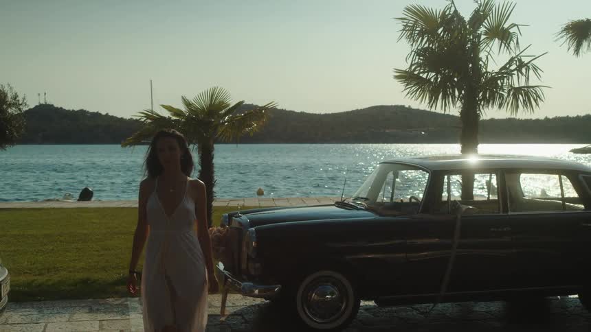 Woman walks across path by parked cars with blue water in the background