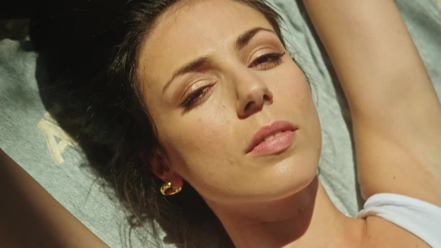 Close up of the face of a young woman laying over a blanket outdoors looking at the camera