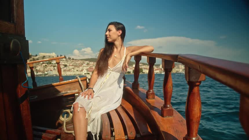 A woman wearing a sundress is relaxing on a bench on a boat sailing in the water