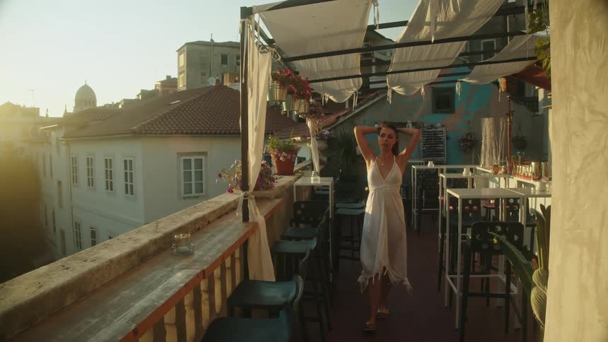 Woman wearing a white dress walking on the balcony of a building on an european city