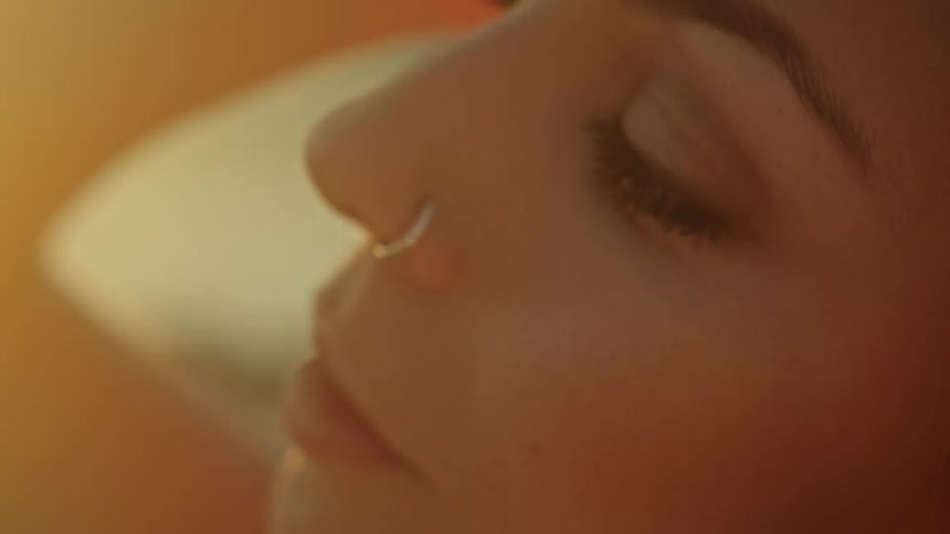 Woman with makeup and nose piercing looks at camera as the sun shines on her face