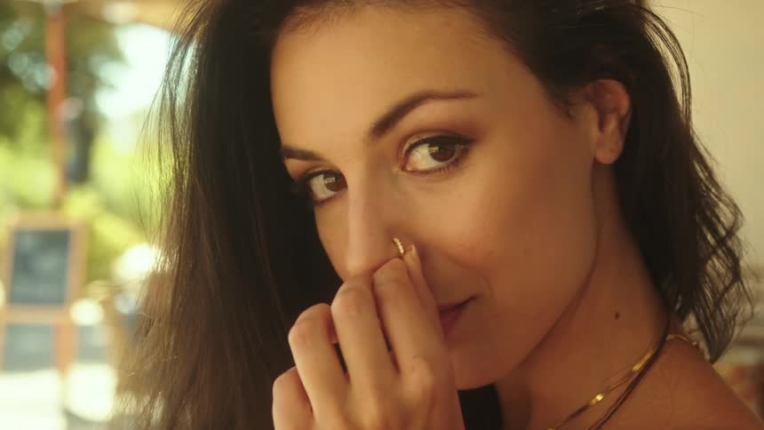 Woman with dark hair and necklace wears nose piercing looking at camera smiling