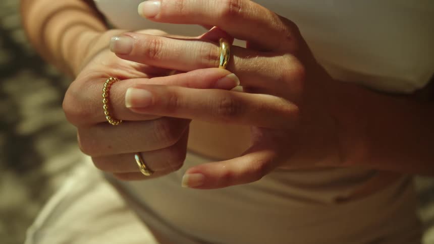 Young woman wearing a white dress puts a golden ring on her finger
