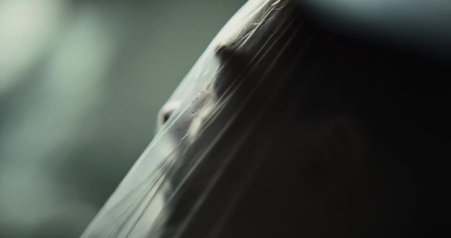 A woman moves her head under a translucent plastic bag in front of a dark background