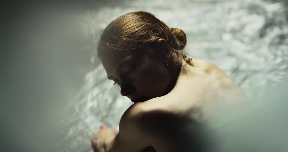 Naked woman sitting on the ground of a room wrapped in plastic looks at the camera
