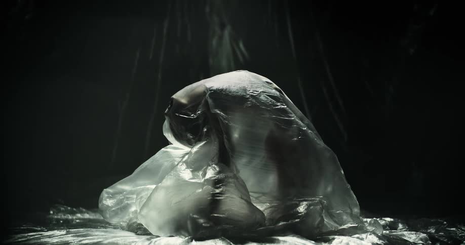 A woman arching her back under a translucent plastic bag in front of a dark background