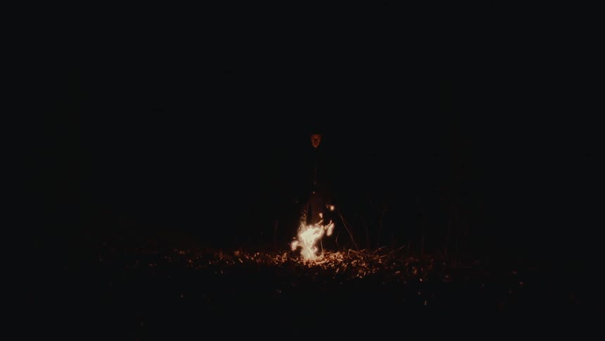 A man is outdoors near a bonfire during the night time