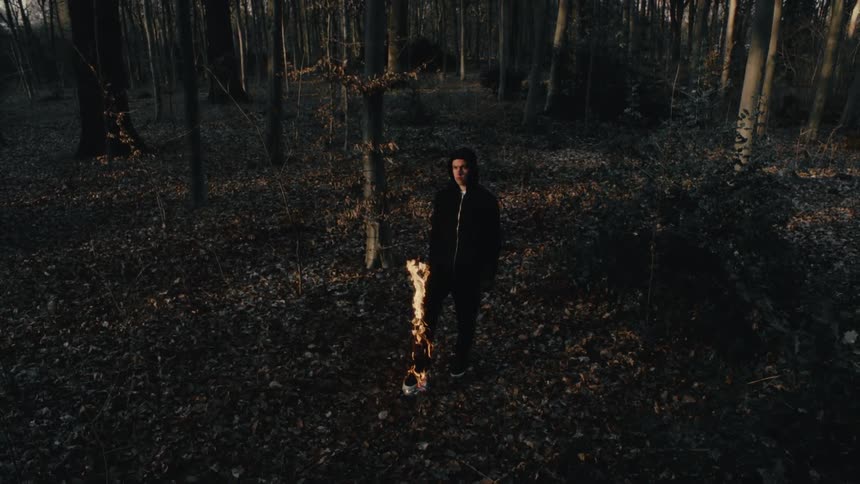 Flames travel up a mans leg as he stands in the woods